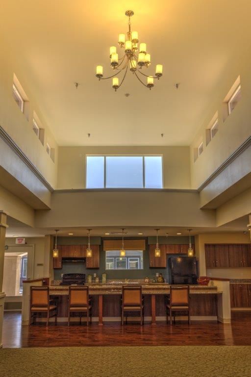A modern kitchen with an open layout, featuring a high ceiling and a central island under a chandelier.