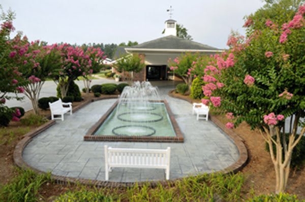 A serene garden setting featuring a central fountain, surrounded by blooming flowers and white benches.