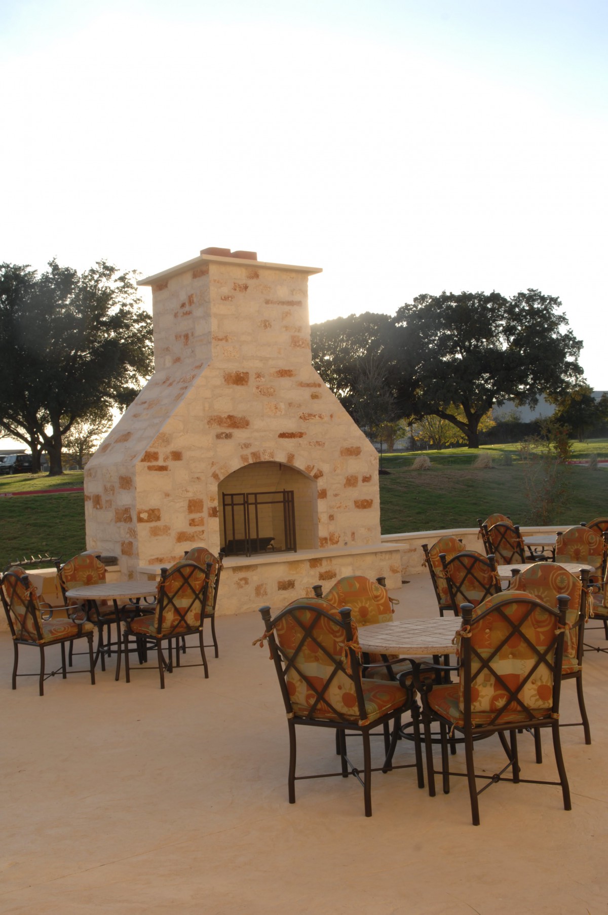 An outdoor patio with a stone fireplace, surrounded by tables and chairs.