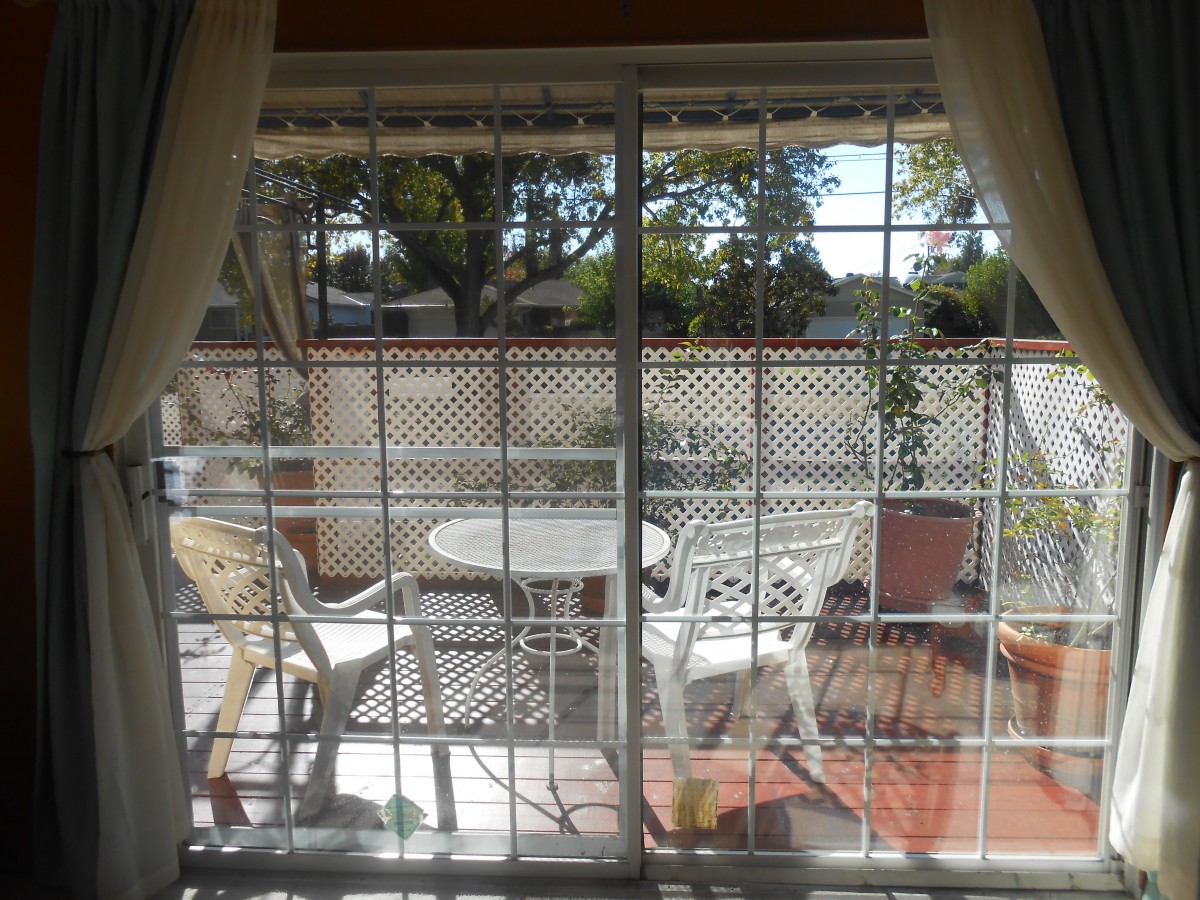 A sunny patio with white furniture viewed through a glass door.