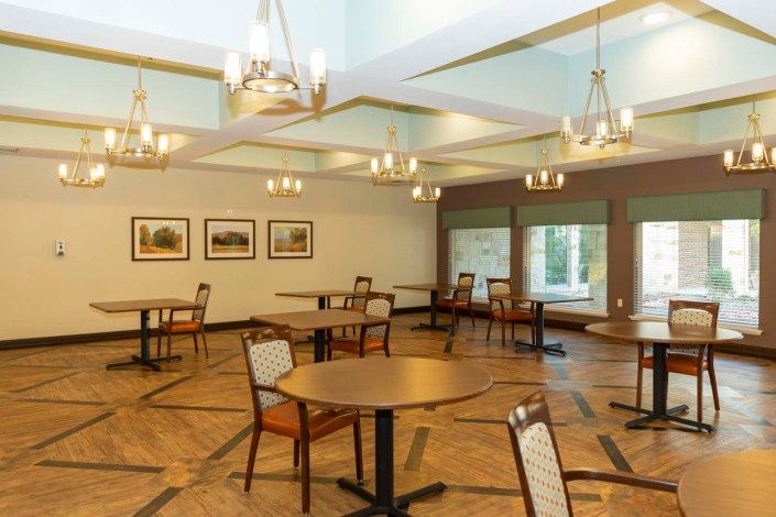 An empty dining area with tables and chairs arranged under stylish chandeliers.