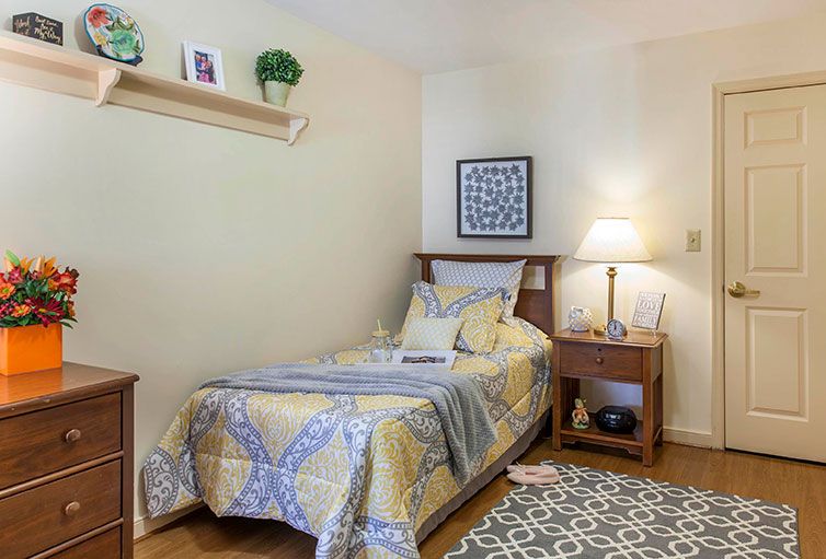 A cozy bedroom with a single bed, decorated with a lamp and wall art.