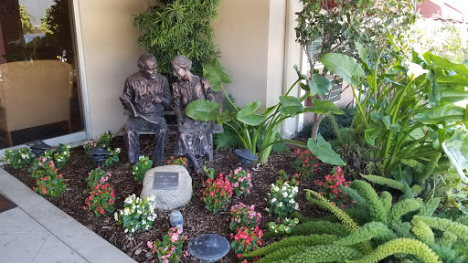 A serene garden featuring a beautiful sculpture of two figures amidst vibrant flowers and lush plants.