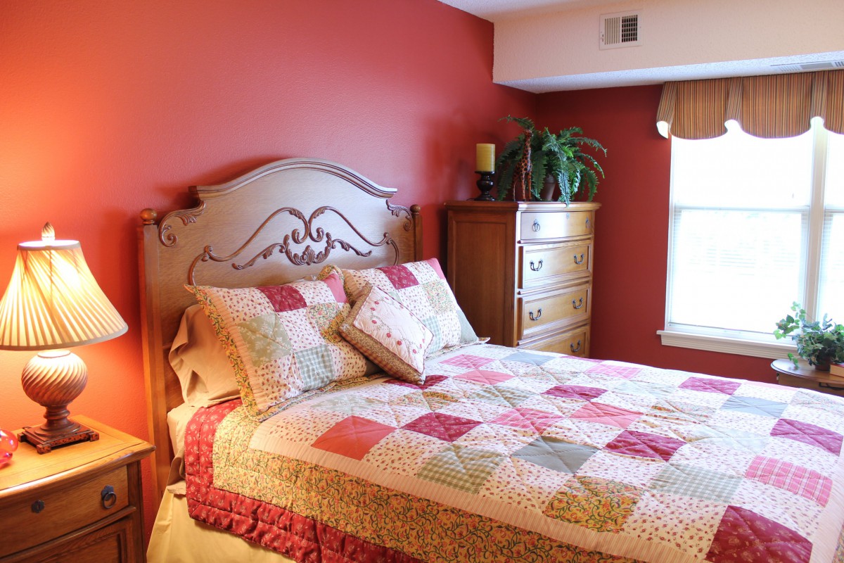 A cozy bedroom with a colorful quilt and red accent wall.