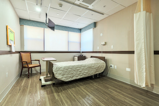 A clean and well-lit hospital patient room featuring a bed and seating area.