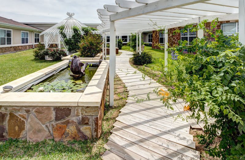 A serene garden with a shaded walkway, pergola, and pond.