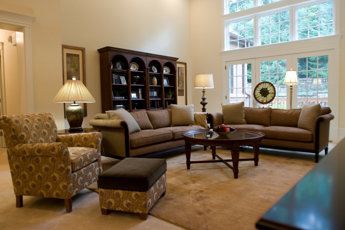 A cozy living room with comfortable sofas, a wooden coffee table, and a tall bookshelf near large windows.