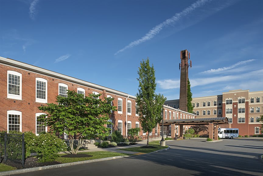 A brick building with a tall chimney, surrounded by trees under a clear blue sky.