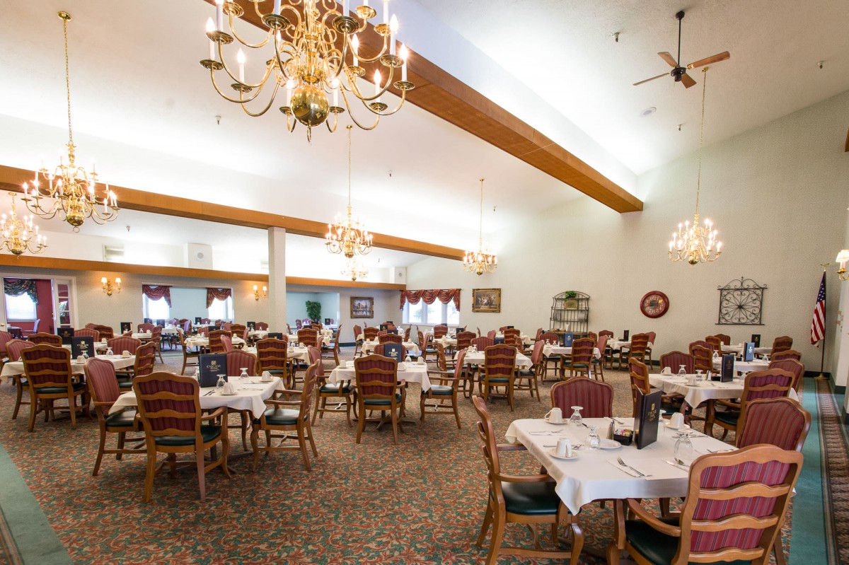 An elegant dining room with multiple tables set up and ornate chandeliers hanging from the ceiling.