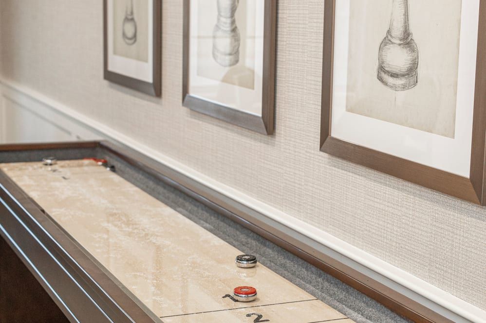 An indoor shuffleboard table with framed artwork on the wall.