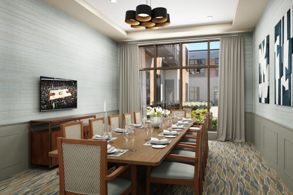A modern dining room with a large table set for a meal, featuring stylish lighting and a window view.