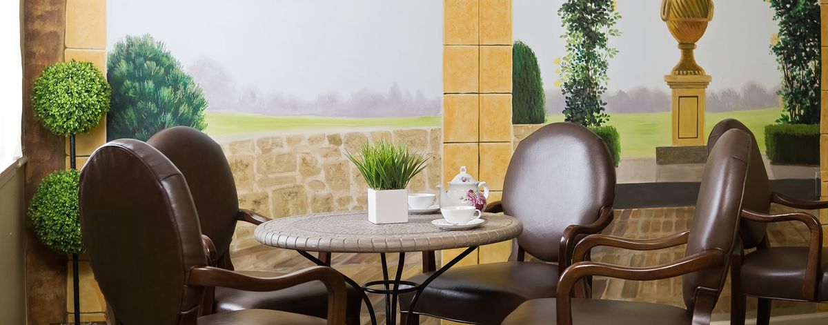 A cozy patio setting featuring a small round table with chairs, adorned with a tea set and potted plant.