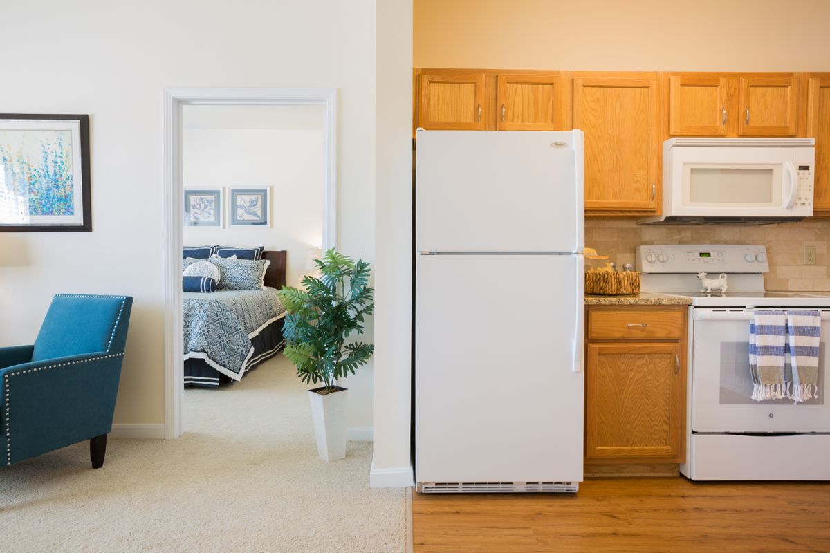 An interior view showcasing a kitchen with wooden cabinets and a white fridge adjacent to a bedroom with neutral colors.