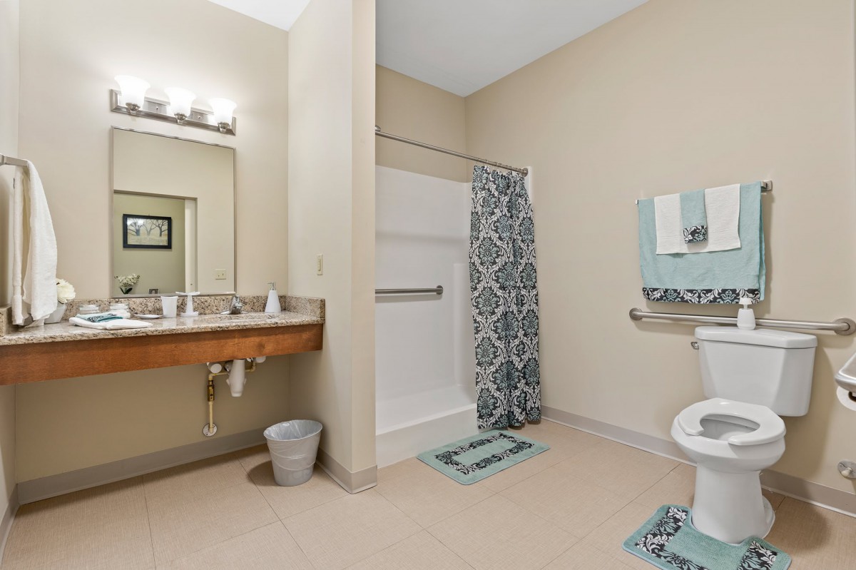 A clean and modern bathroom featuring a shower area with a patterned curtain, a large mirror above the sink, and neatly arranged towels.