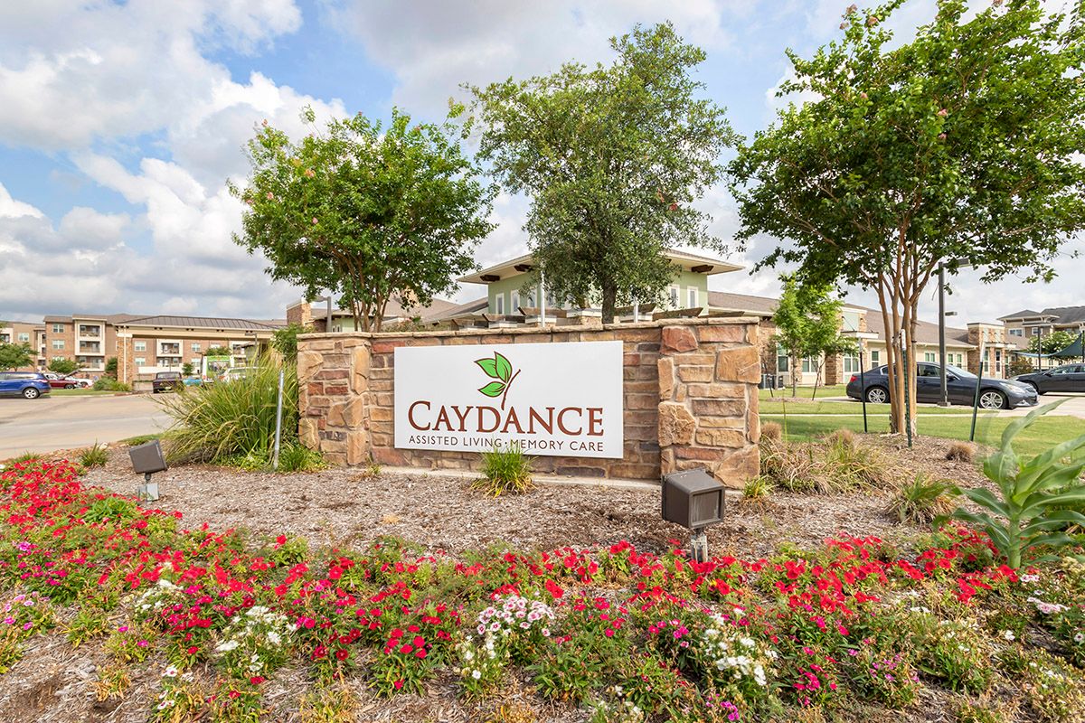 An entrance sign for a place called 'Caydance' surrounded by well-maintained landscaping, including trees and flowers.