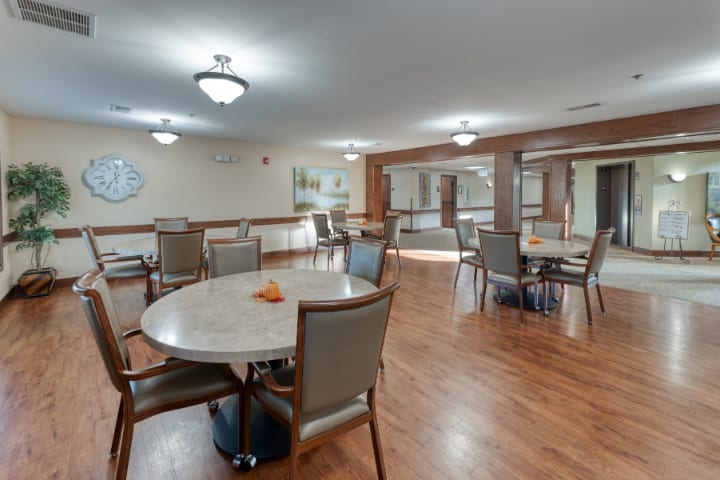 A spacious dining area with round tables and cushioned chairs on a wooden floor.
