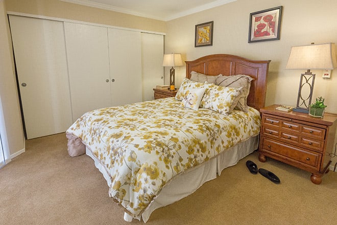 A cozy bedroom with a floral-patterned bedspread, wooden furniture, and decorative wall art.
