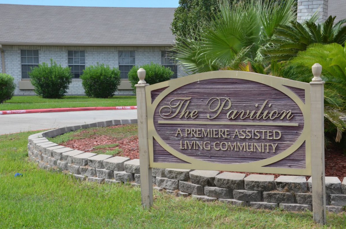 Sign for 'The Pavilion', a premiere assisted living community, set in a landscaped area with a building in the background.