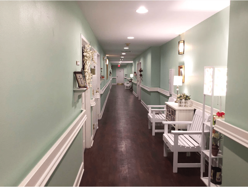 A long hallway with light green walls, decorated with chairs and lamps.