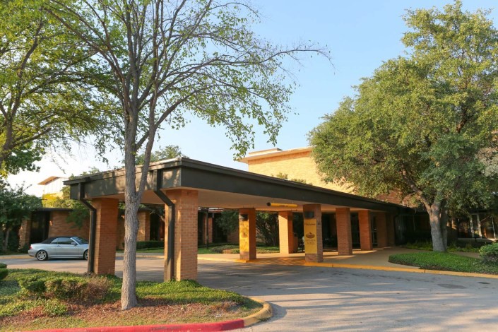 Entrance of a hotel with trees and a driveway on a sunny day.