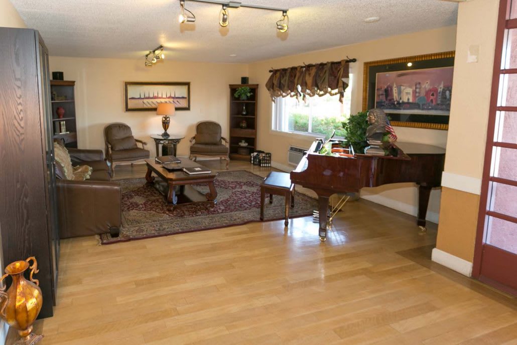 A spacious living room with hardwood flooring, featuring comfortable seating, a grand piano, and a decorative rug.