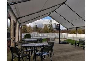 A covered patio area with tables and chairs, overlooking a backyard with a basketball hoop.
