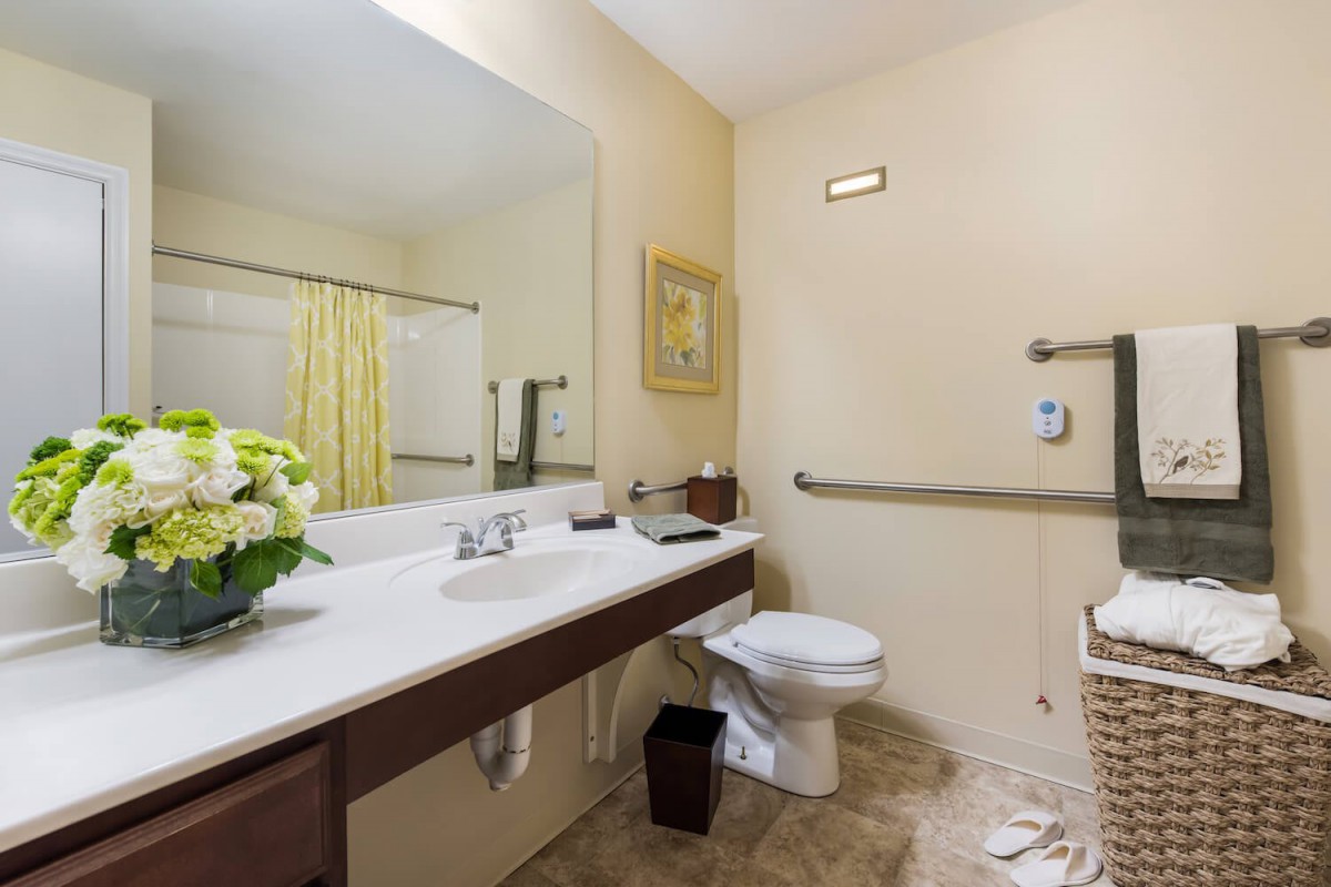 A clean and spacious bathroom with a large mirror, sink, toilet, and a decorative bouquet of flowers.