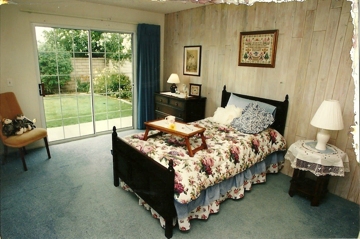 A cozy bedroom with a floral-patterned bedspread and a sliding glass door leading to the garden.