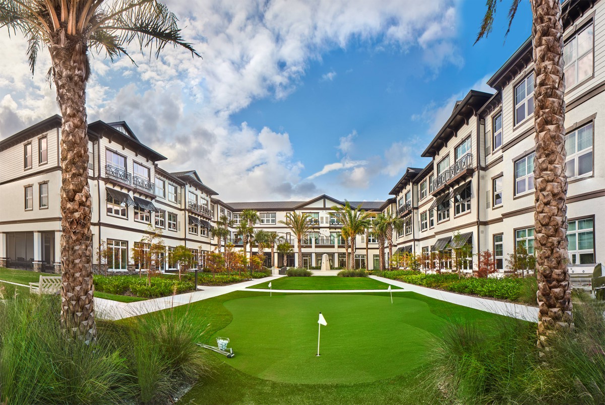 A modern residential building with a landscaped courtyard and mini golf area under a partly cloudy sky.