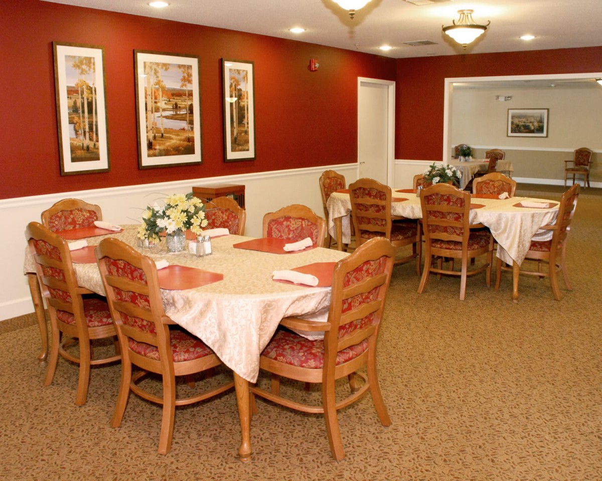 A cozy dining room with neatly set tables and warm, red walls adorned with framed paintings.