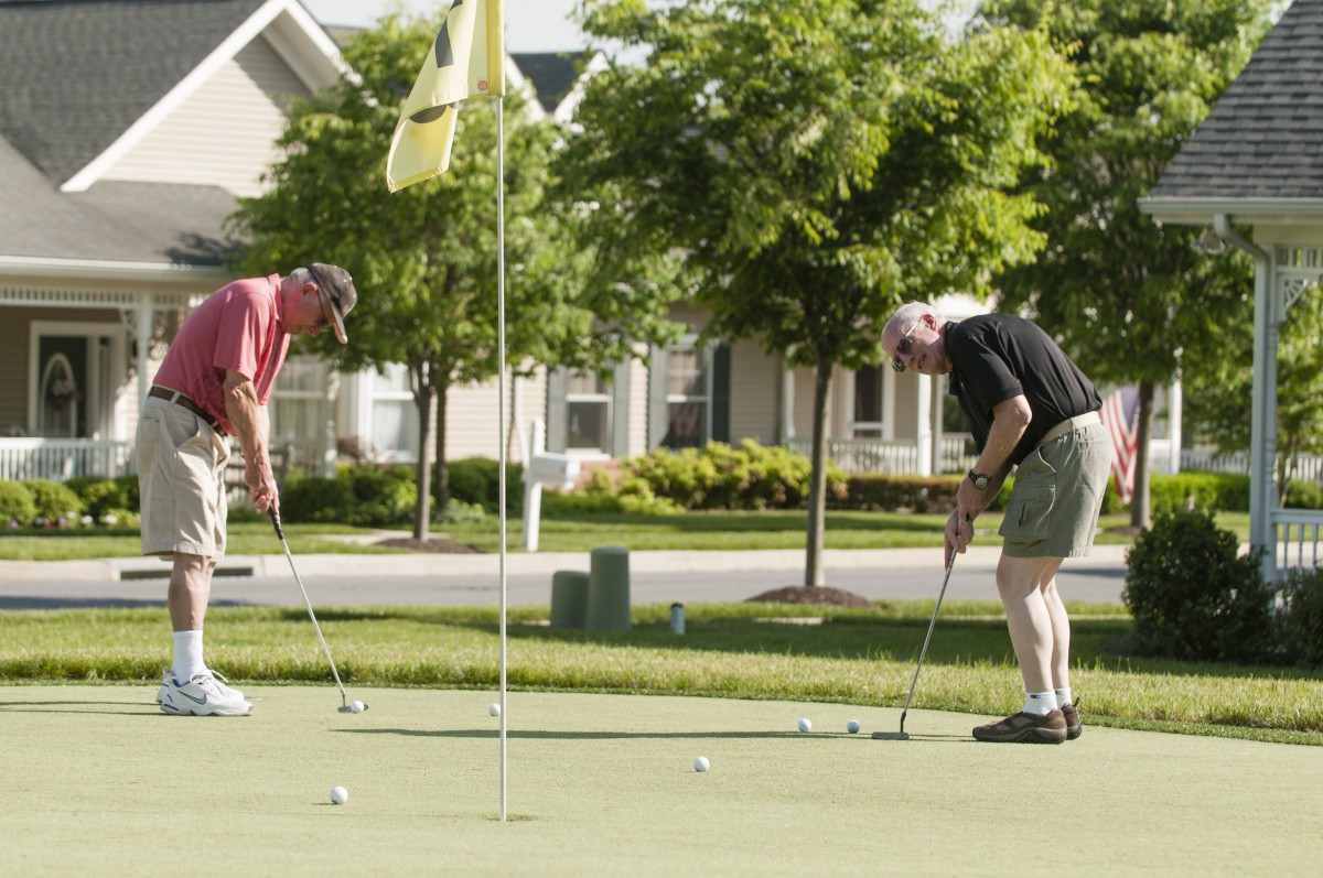 Two golfers on a putting green practicing their shots on a sunny day.