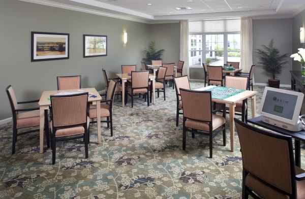 A well-lit dining room with neatly arranged tables and chairs, featuring a patterned carpet and wall art.