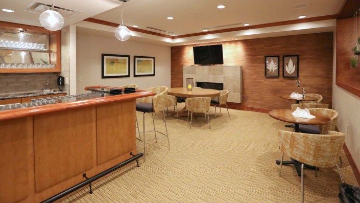 A modern living room with bar and seating area, featuring wood paneling and a fireplace.