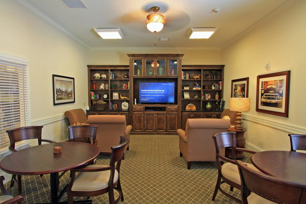 Cozy living room with a television and bookshelves, featuring comfortable chairs and elegant decor.