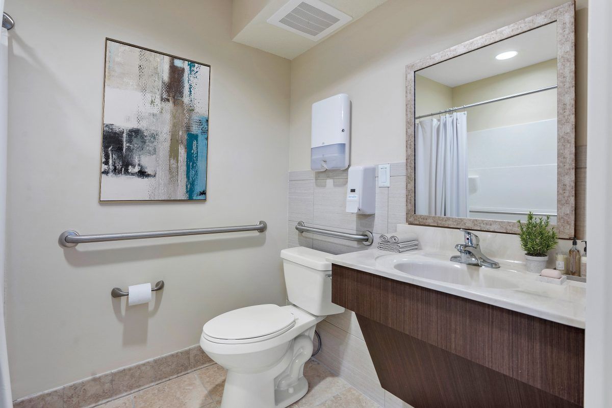 A modern, clean bathroom with accessibility features, including a toilet, sink, and mirror.