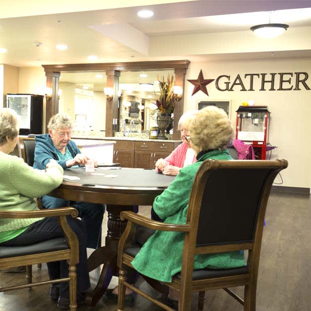 A group of elderly people sitting around a table in a common area, engaged in conversation.