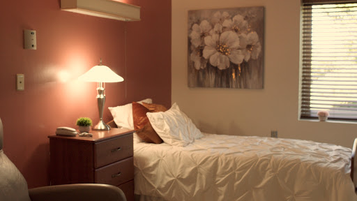 A cozy bedroom featuring a neatly made bed, a stylish lamp, and floral artwork on the wall.