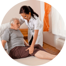 A caregiver assists an elderly man with physical therapy at home.