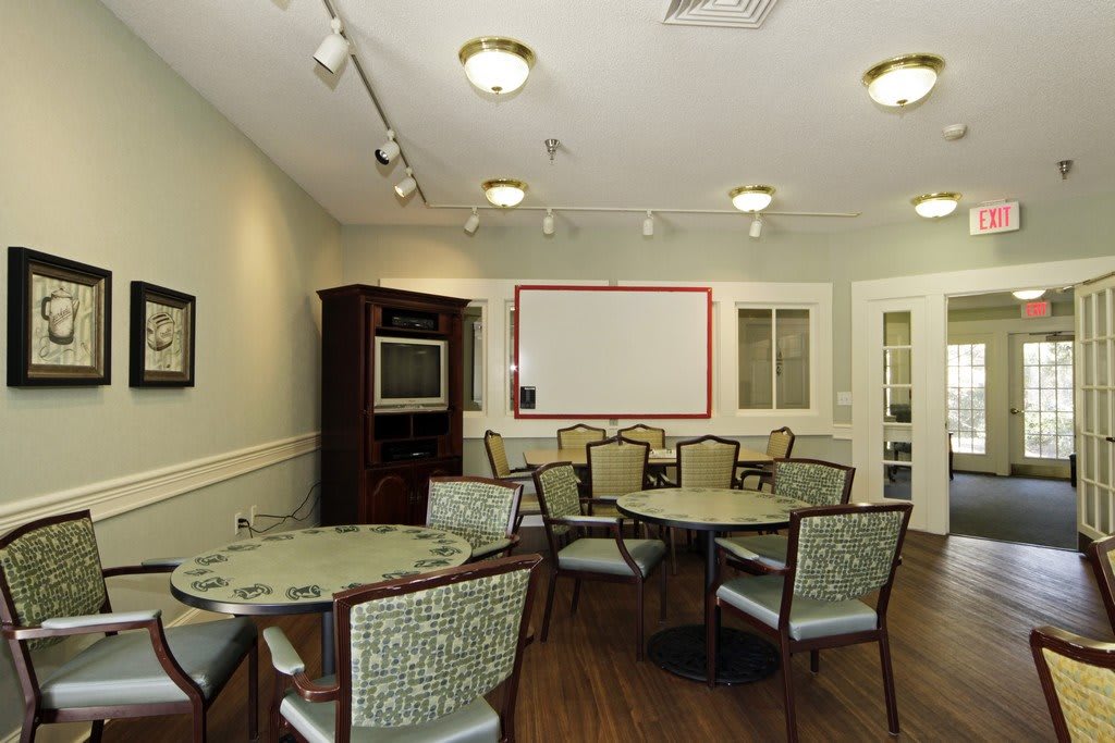 A well-lit meeting room with multiple tables, chairs, and a whiteboard.