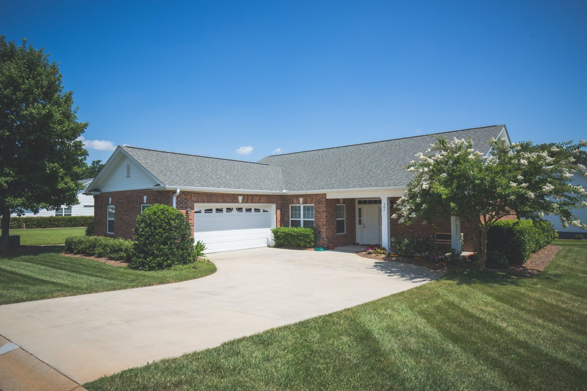 A single-story suburban house with a driveway and a well-maintained lawn under a clear blue sky.