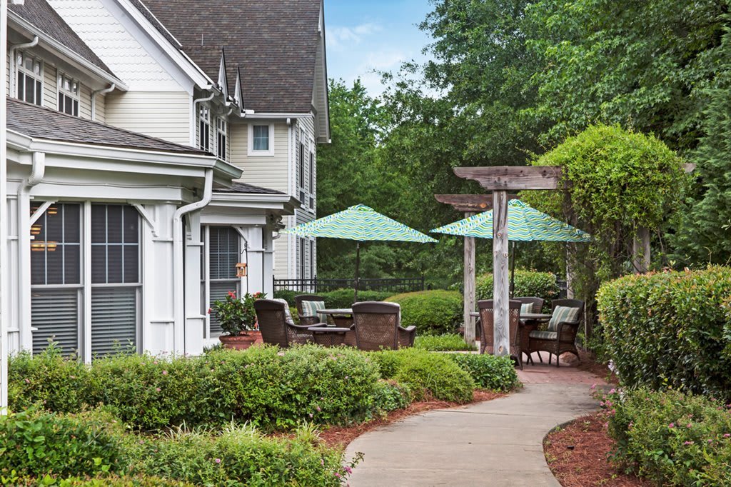 A charming outdoor patio area with seating and umbrellas next to a house, surrounded by lush greenery.