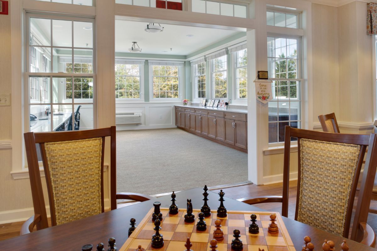 A cozy game room with a chess set ready for play, overlooking a bright sunroom.