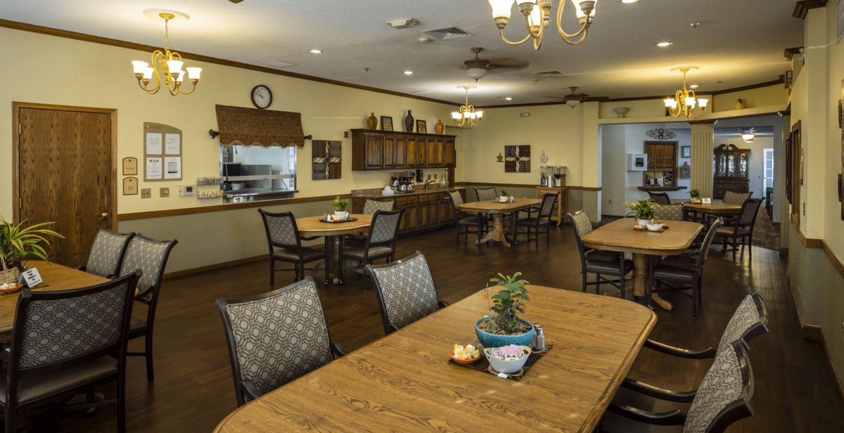 A cozy dining room with several tables and chairs, featuring warm lighting and a wooden floor.