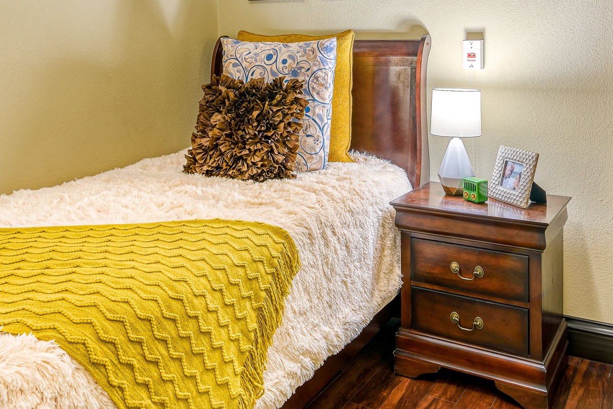 A cozy bedroom with a neatly arranged bed and an elegant nightstand with a lamp.