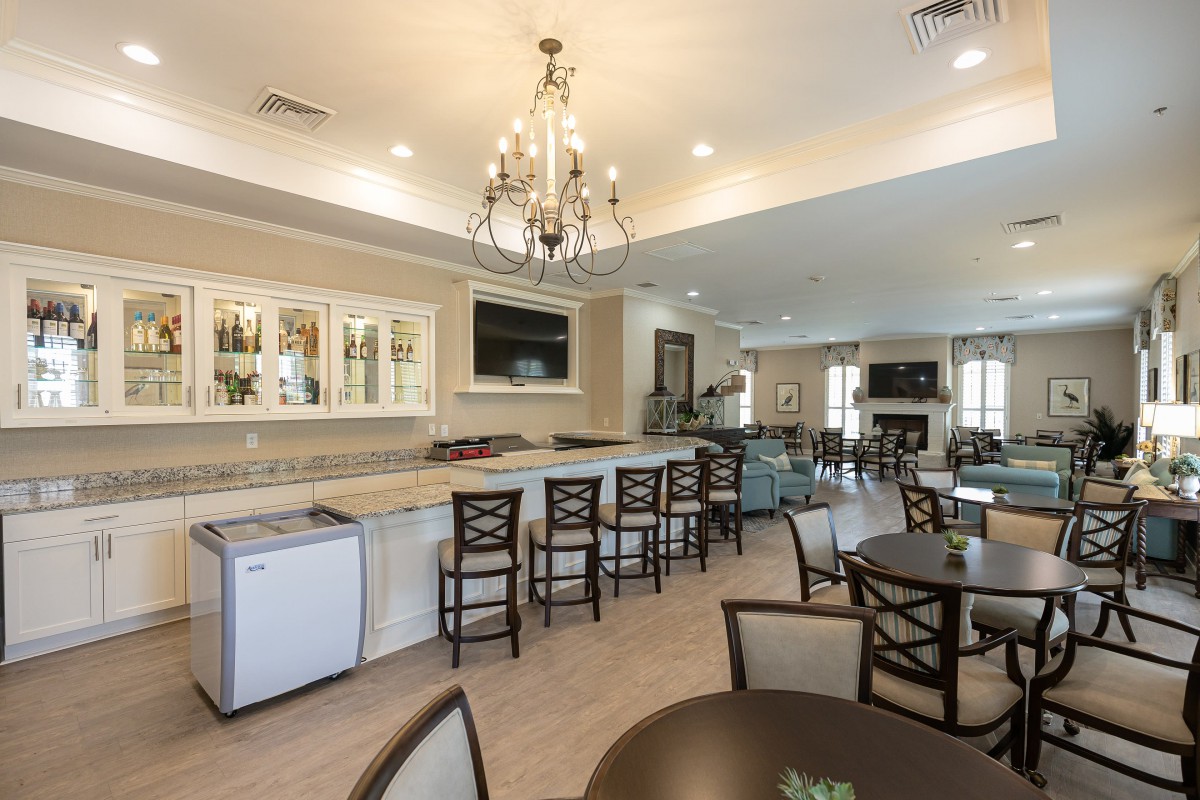 A spacious modern kitchen and dining area featuring a bar with high chairs, a chandelier, and comfortable seating.