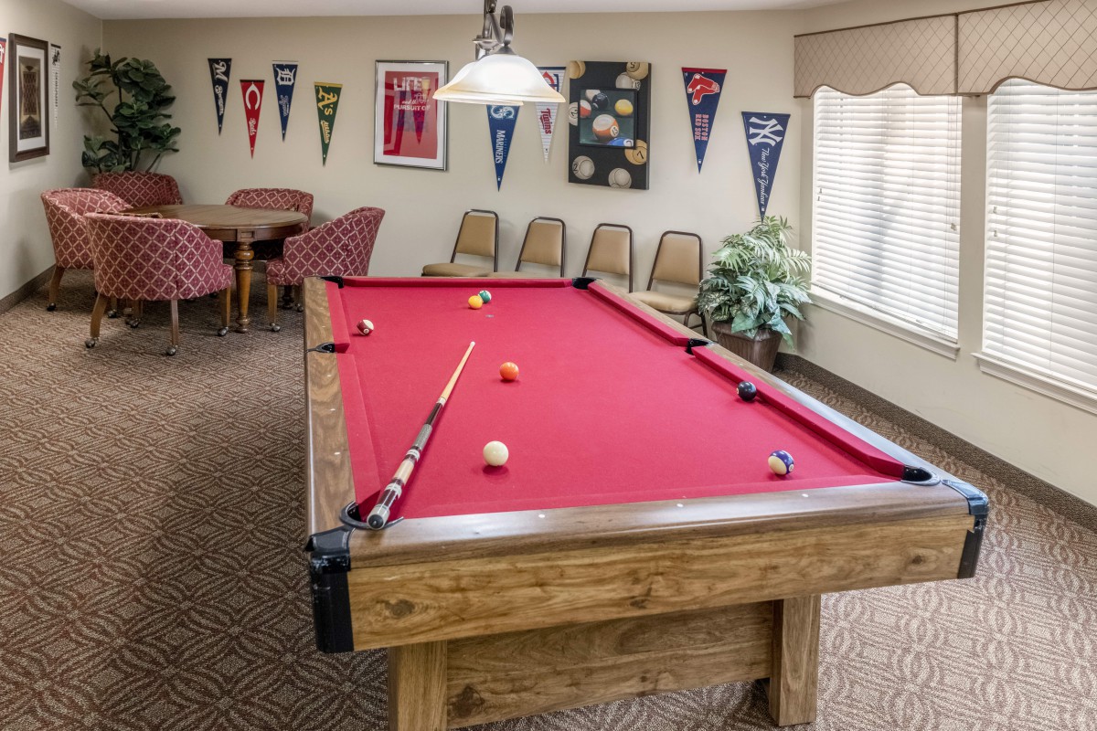 A cozy game room featuring a pool table with red felt, surrounded by chairs and decorated with pennants.