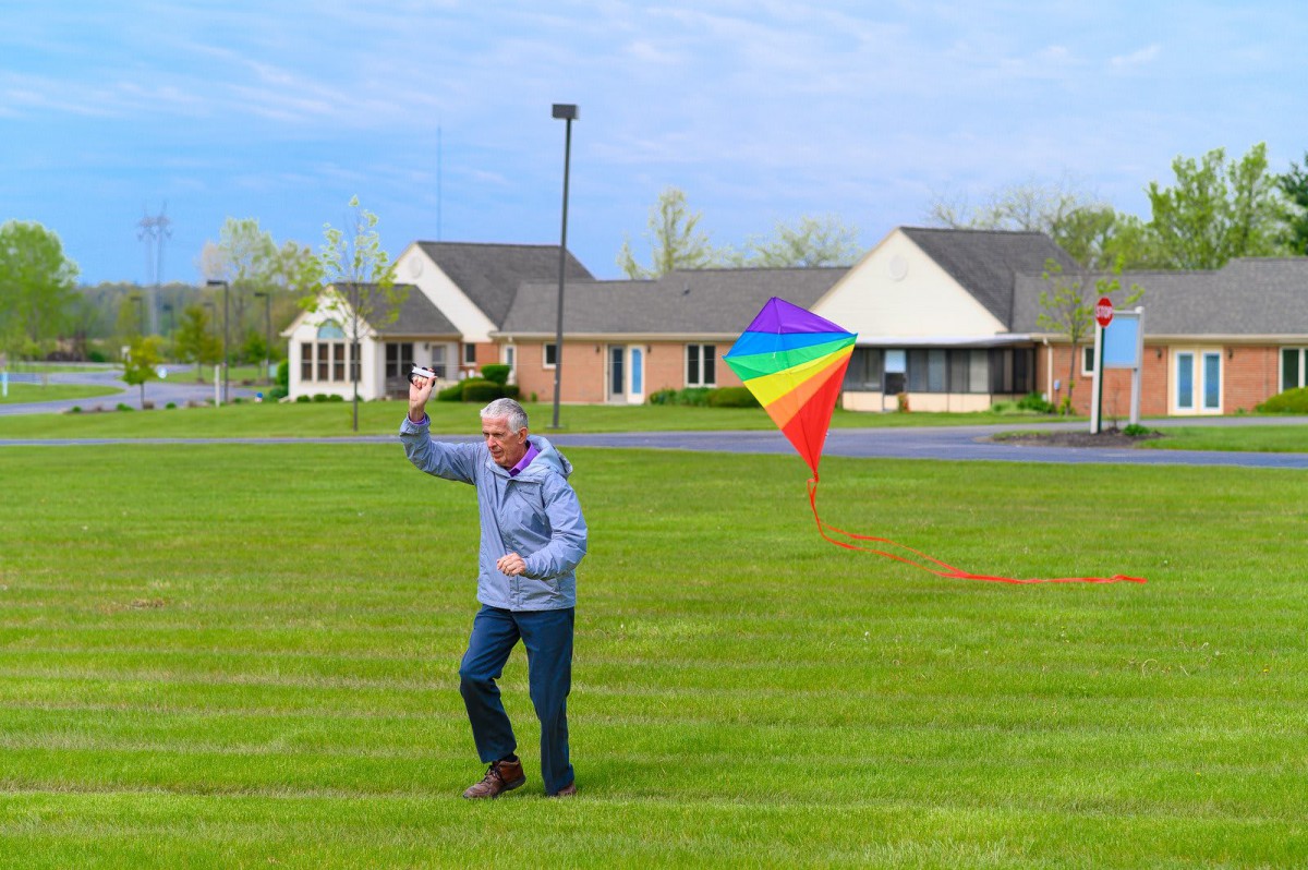 An elderly person enjoying a day outdoors, flying a colorful rainbow kite on a grassy field.