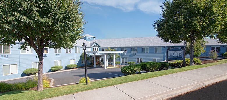 Exterior view of a hotel with a driveway and surrounding greenery under a clear blue sky.
