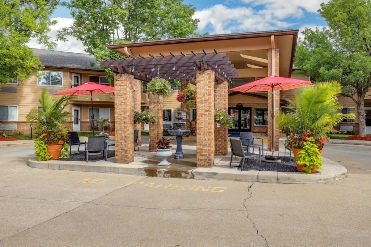 A charming outdoor patio area featuring a pergola, fountain, and seating with red umbrellas.