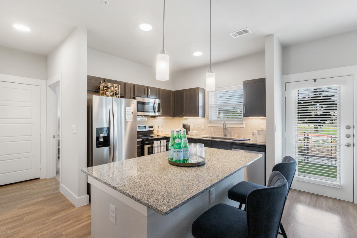 A modern kitchen with granite countertops, stainless steel appliances, and pendant lighting.